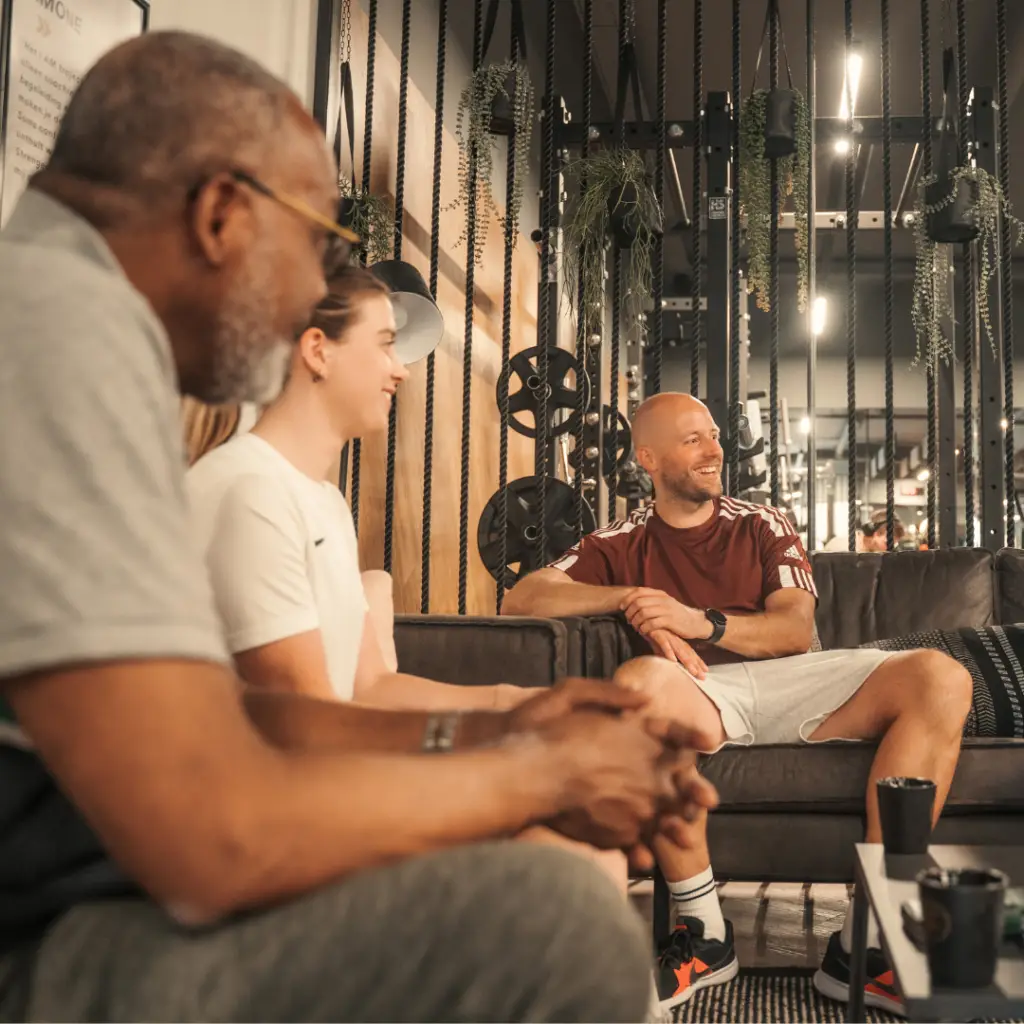 Drie leden ontspannen zich en maken een praatje op comfortabele banken in een lichte, moderne lounge bij COMMIT Health Club Utrecht. Met ultramoderne fitnessapparatuur en weelderig groen op de achtergrond kletsen ze gezellig en glimlachen ze onder het genot van een kopje koffie. Deze uitnodigende omgeving weerspiegelt de warme, persoonlijke sfeer van onze premium health club – waar elke gast zowel deskundige begeleiding als oprechte momenten van ontspanning geniet.