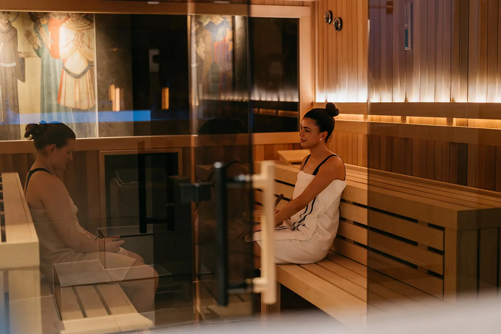 In onze moderne sauna bij COMMIT Health Club Utrecht ontspannen twee vrouwen in handdoeken op elegante houten banken, omringd door zacht, uitnodigend licht en smaakvolle wandkunst. Door de strakke glazen deur biedt dit tafereel je een warm kijkje in de rustgevende wellnessfaciliteiten die onze eersteklas sportschoolervaring in Utrecht kenmerken.